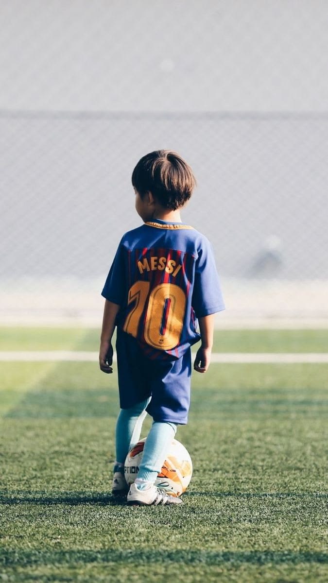Un jeune enfant, de dos, découvre le ballon sur un terrain de football.